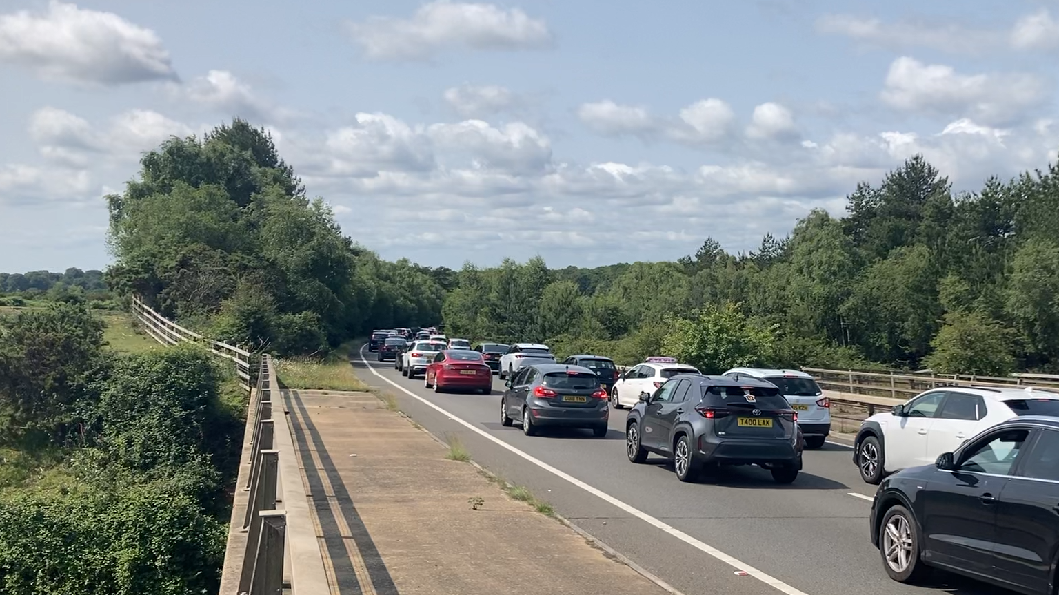 Queues of cars in two lanes driving over a bridge - a large areas of forest can be seen in the distance