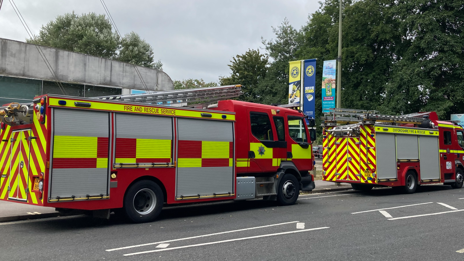 Two fire engines parked on a road in front of a low-level, grey building