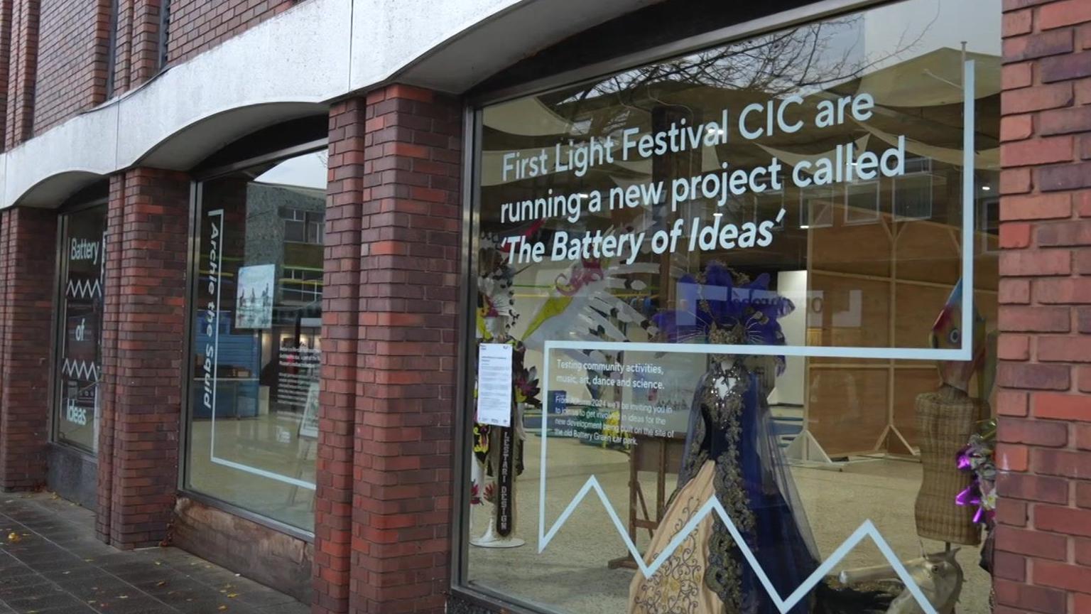 A shop front has large glass windows and printed on one is information about the organisations involved in activities within.