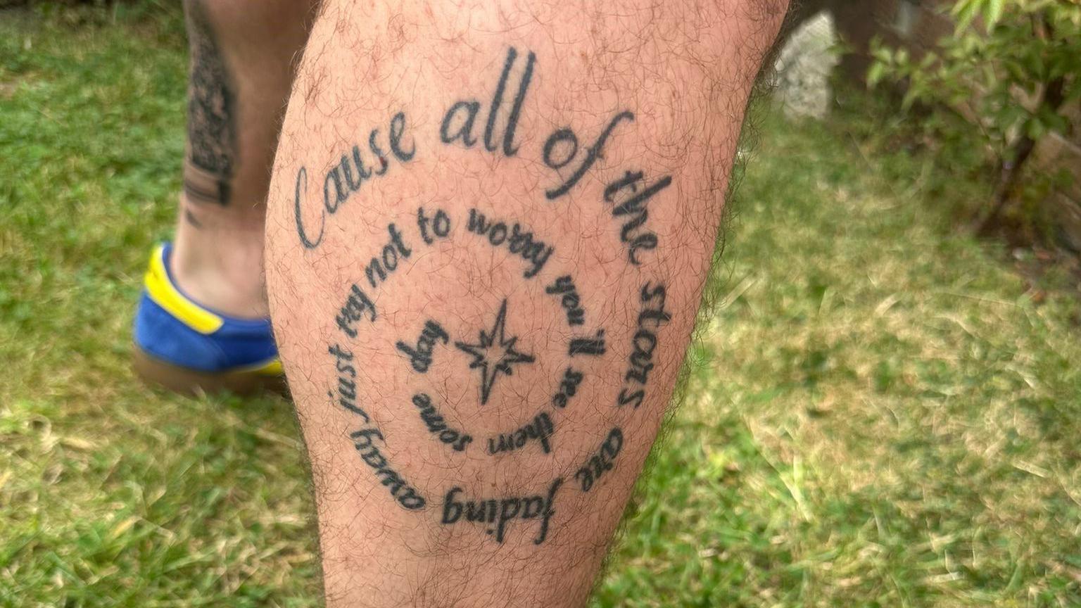 A tattoo of Oasis lyrics in a concentric circle with a star at the centre, reading "cause all of the stars are fading away just try not to worry you'll see them some day".