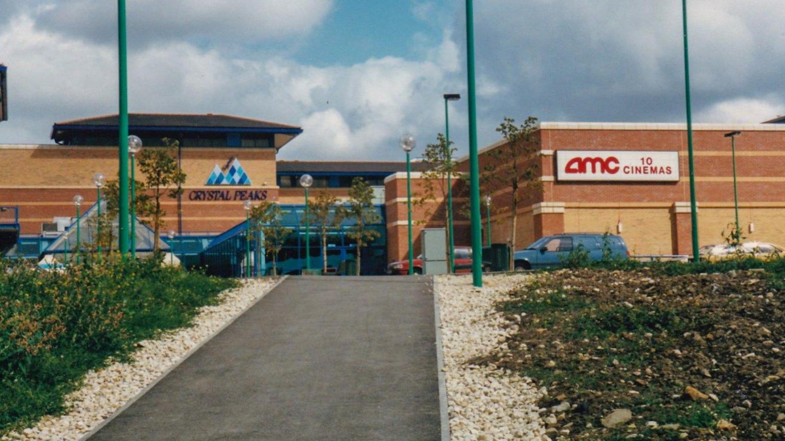 A brown brick shopping centre and car park. A sign reads 'AMC 10 cinema'