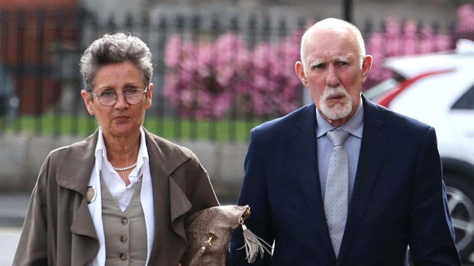 Linda and David Hoy arriving at Newry Crown Court. Linda has short grey hair, wearing glasses, grey waistcoat with white shirt and grey coat. David is bald with white beard, wearing a navy blazer, light blue shirt and light blue tie.