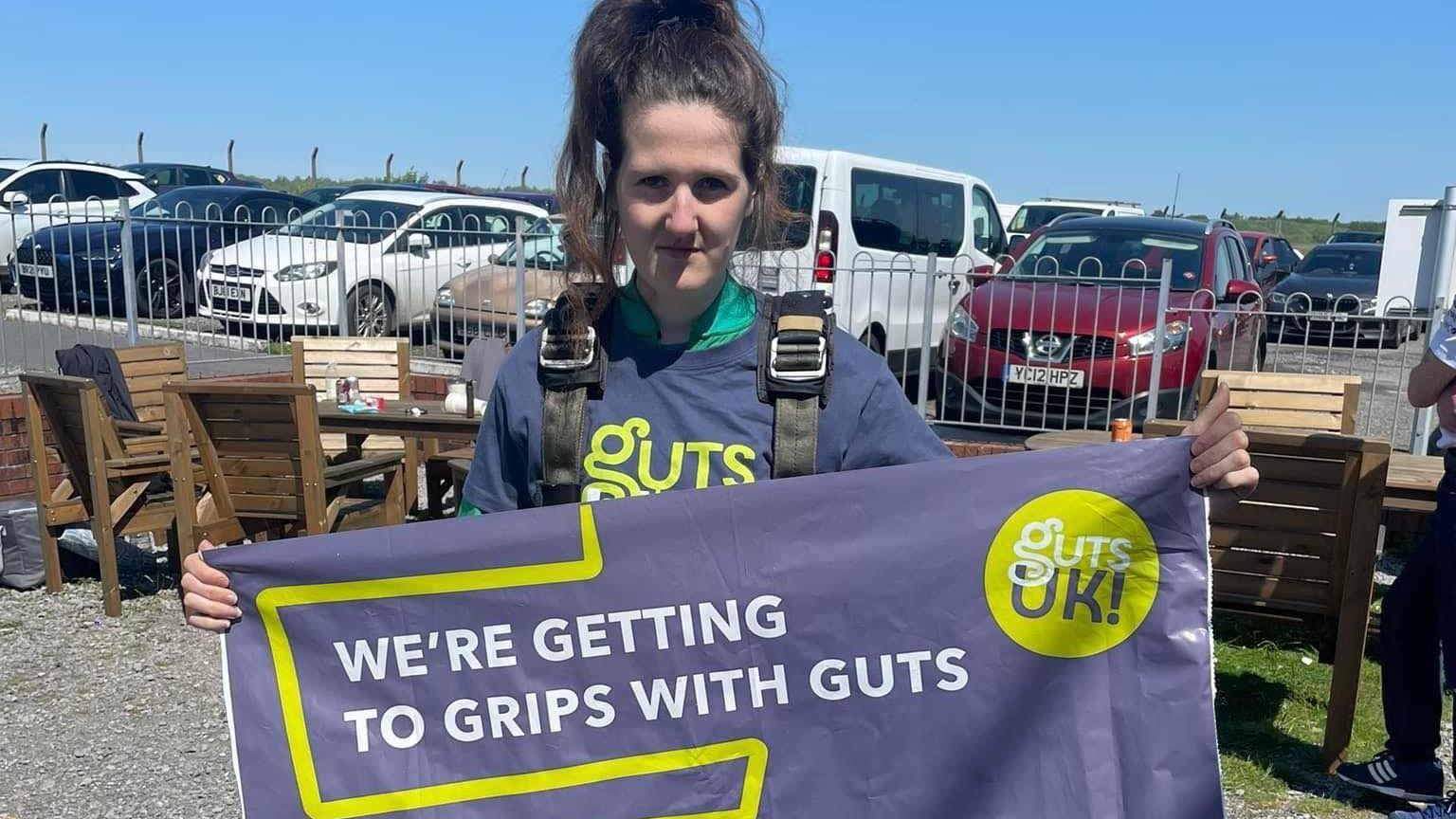 Picture of Luned Davies holding a banner for Guts UK after a skydive 