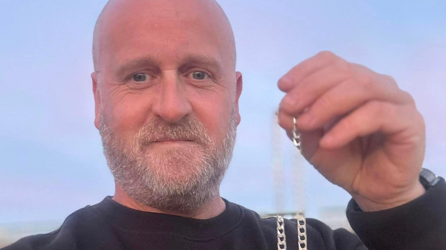 A selfie of Darren Wiles holding up the silver chain.