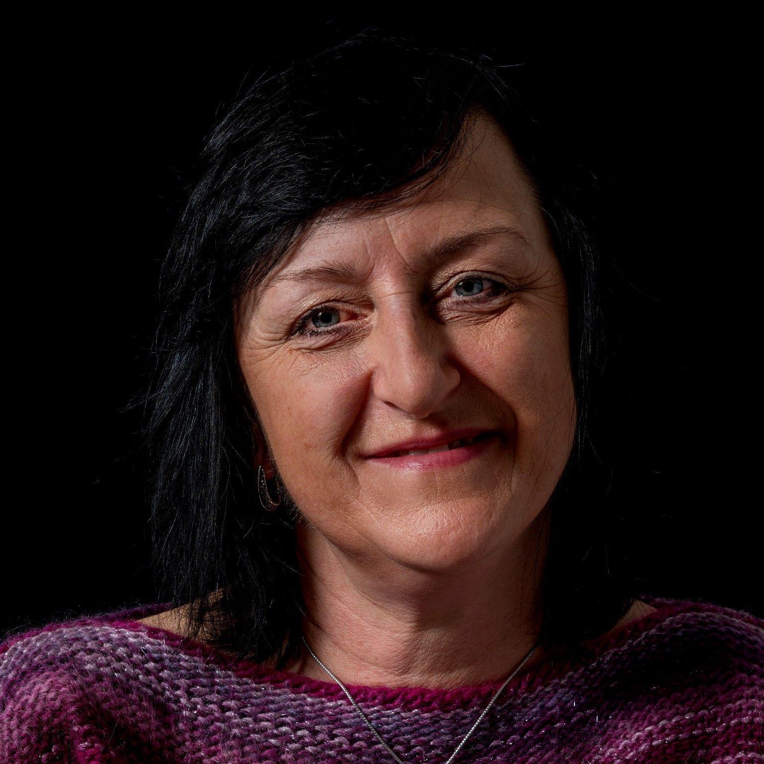 Monika Zywicka, 51, in portrait, wearing a purple jumper in front of a black background