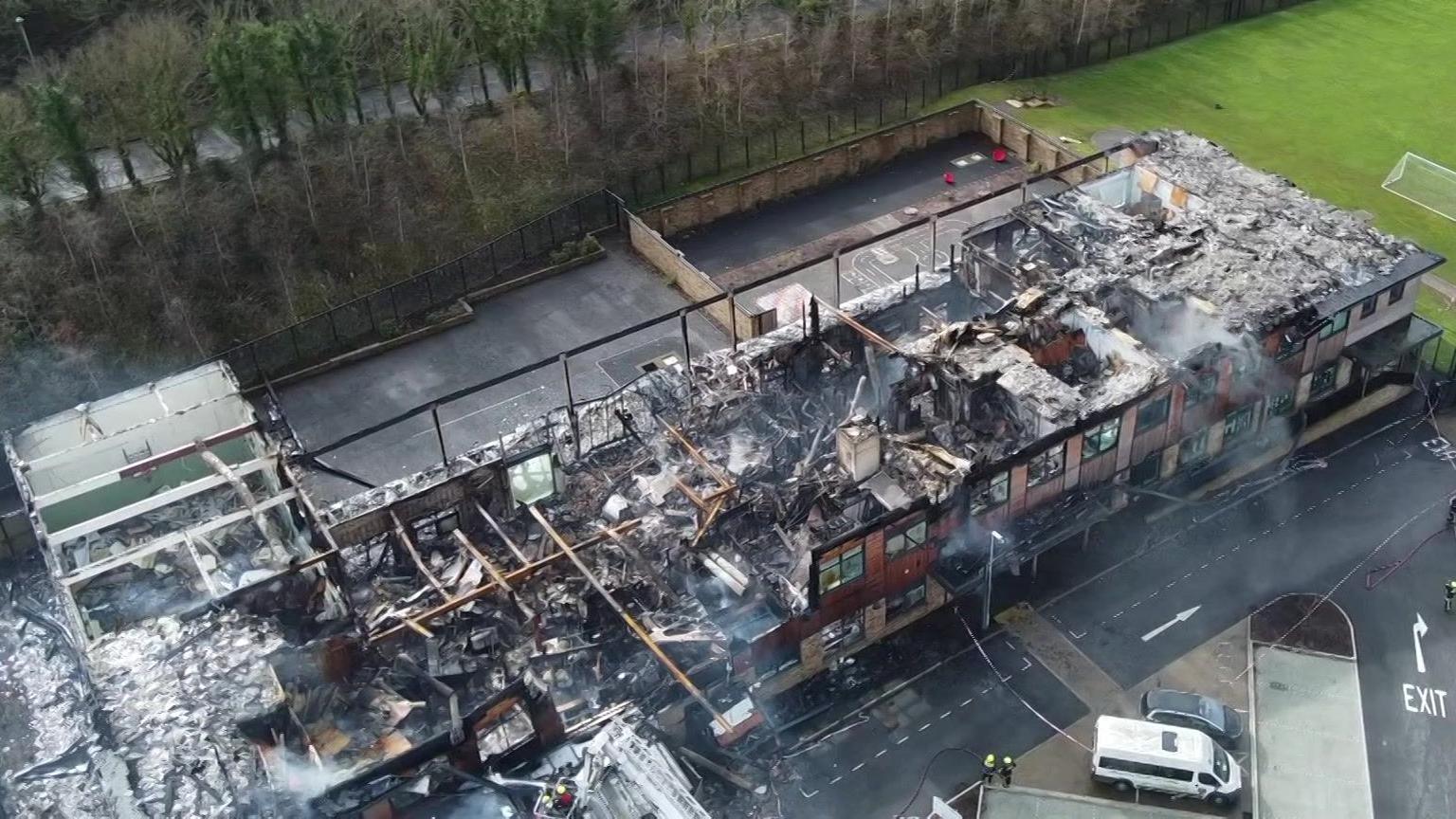 Drone shot showing the inside of a school building following a fire. Smoke is still billowing from the site. The inside of the school has been very badly damaged.