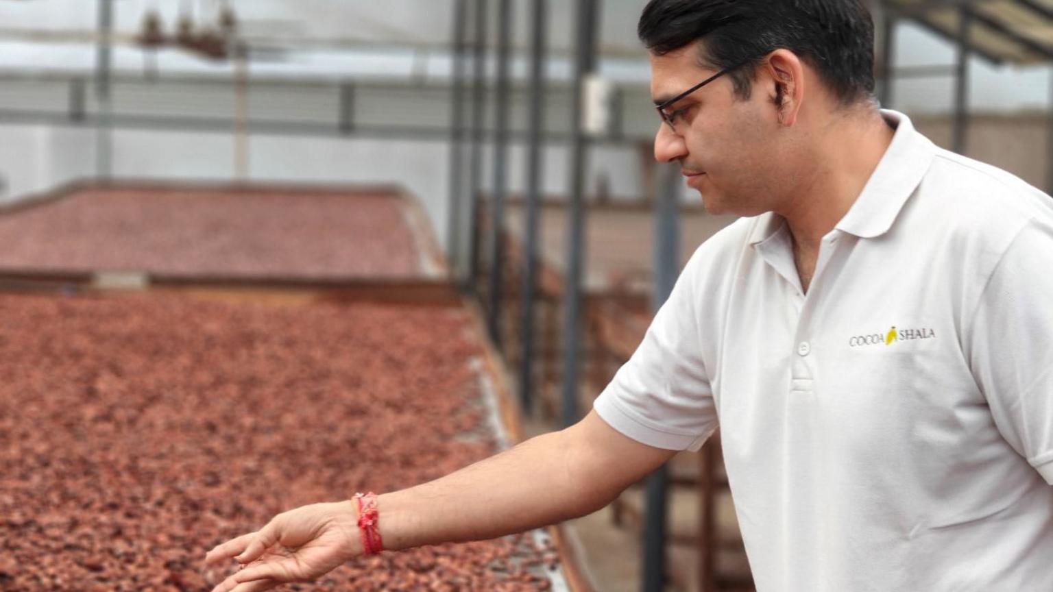 Nitin Chordia, founder of Kocoatrait, reaches forward to handle some drying cocoa beans.