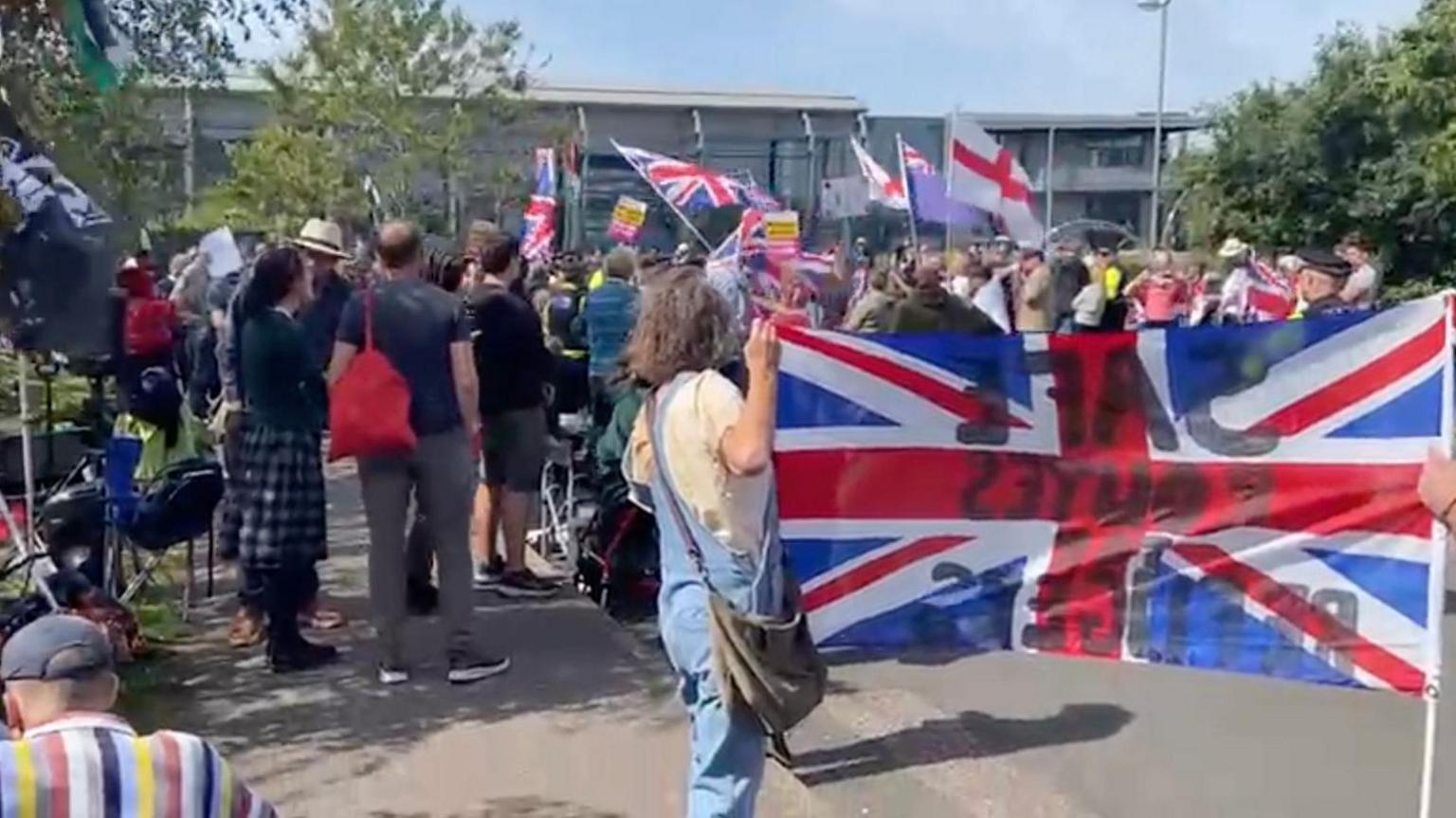 A general shot of the protest and counter-protest taking place outside the hotel with St George's flags and union flags being waved.