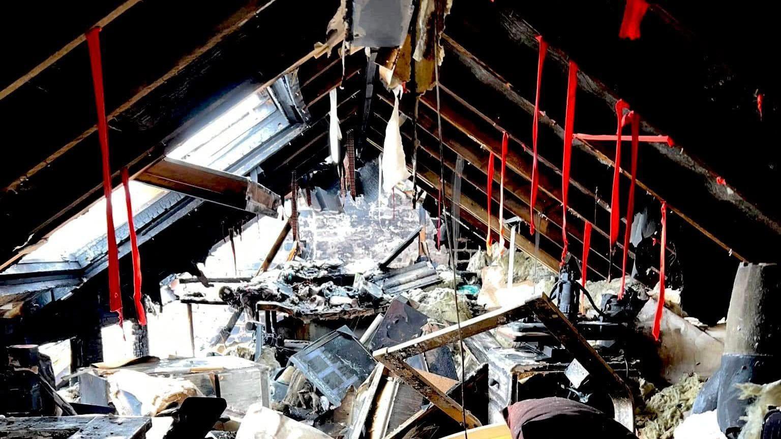 An attic of a house which has been severely damaged and ravaged by fire. All of the items inside are singed and damaged.