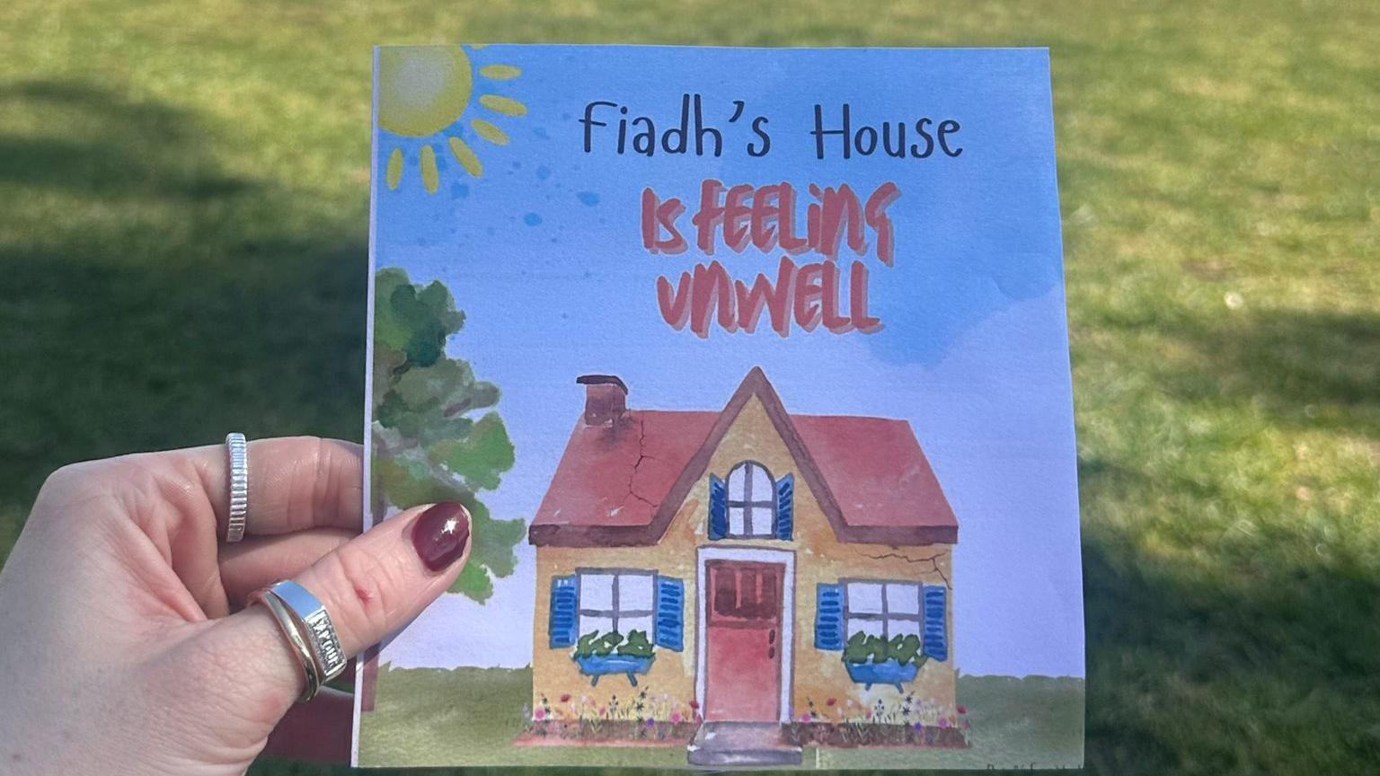 A book with a picture of a house on it with the title: 'Fiadh's House is feeling unwell' accompanied by a picture of a yellow and red house with a number of cracks visible on its front. 