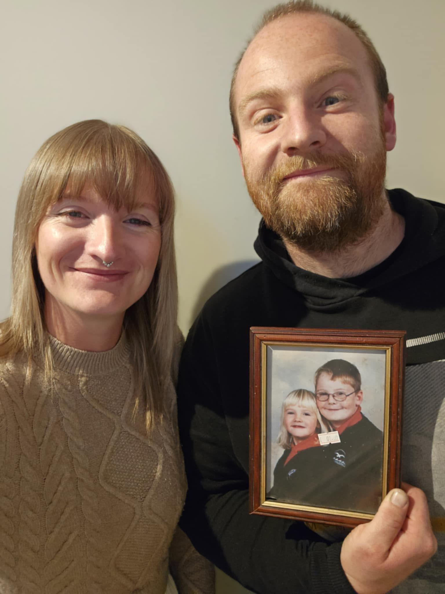 A woman and a man hold a framed photo of two children.