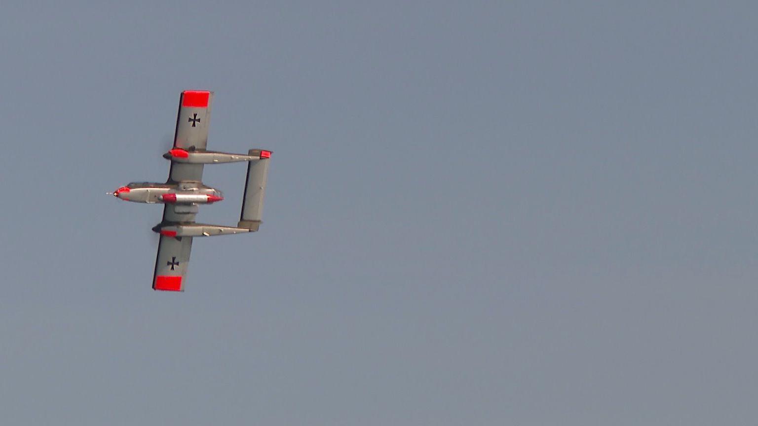 A silver-coloured plane with red markings flying across a blue sky