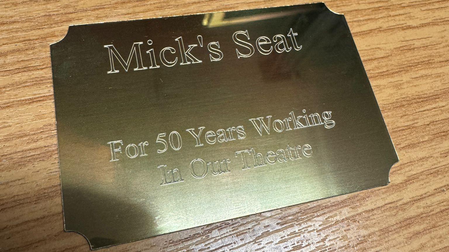 A decorative gold plaque that says "Mick's Seat For 50 years working in our theatre'