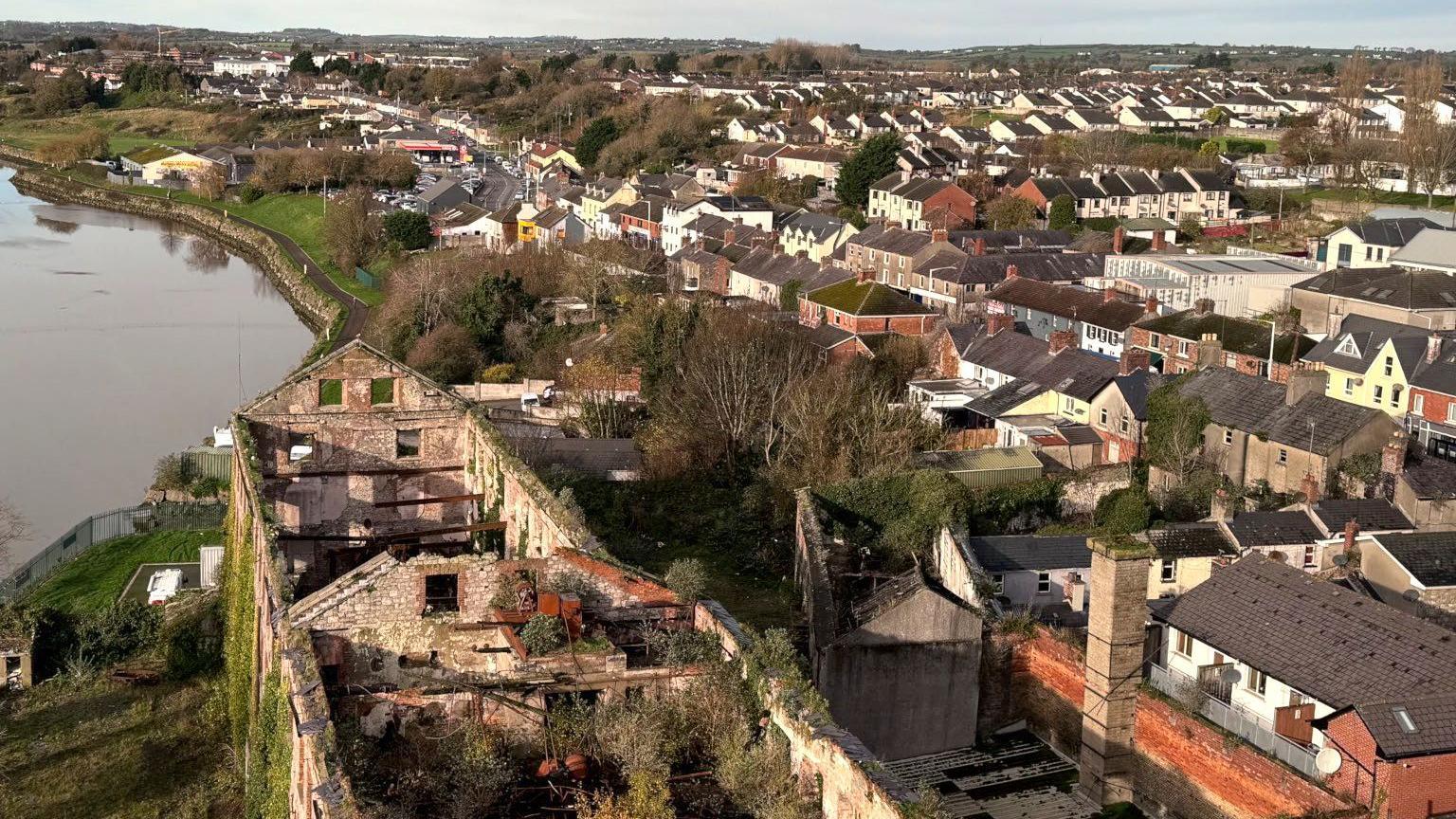 Rows of houses close to a river. In the foreground there is a derelict building