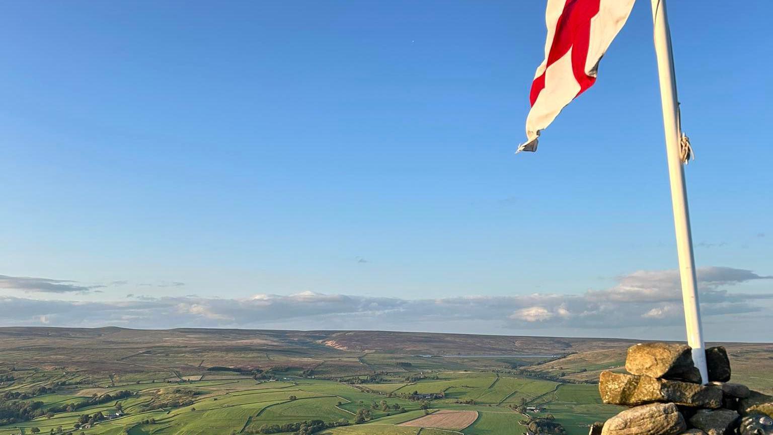 An England flag flies on top of a cairn overlooking dales and moors