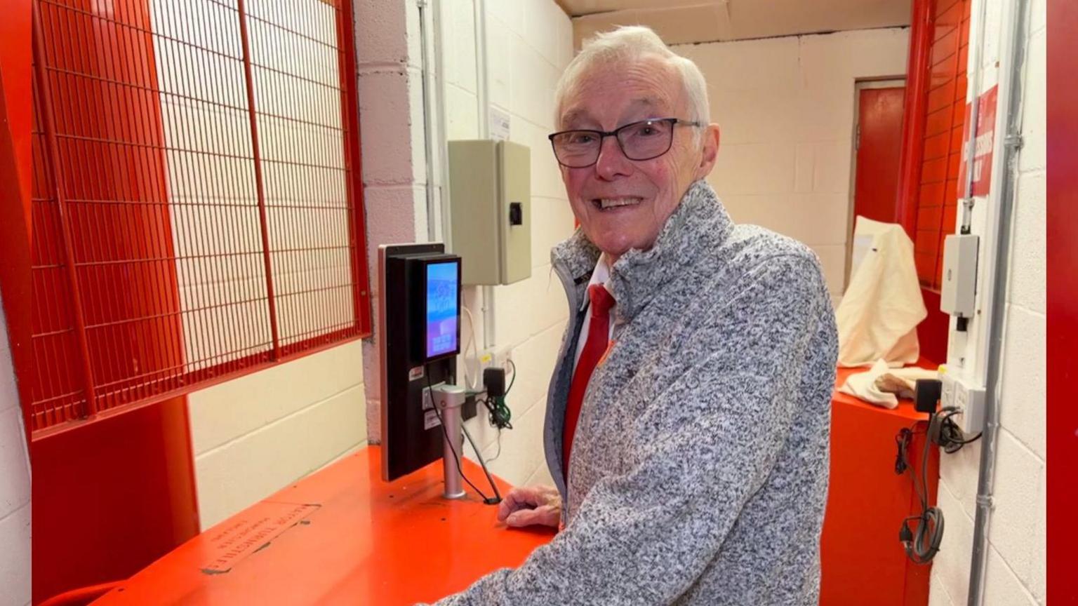 Alan seen stood behind turnstile smiling at camera