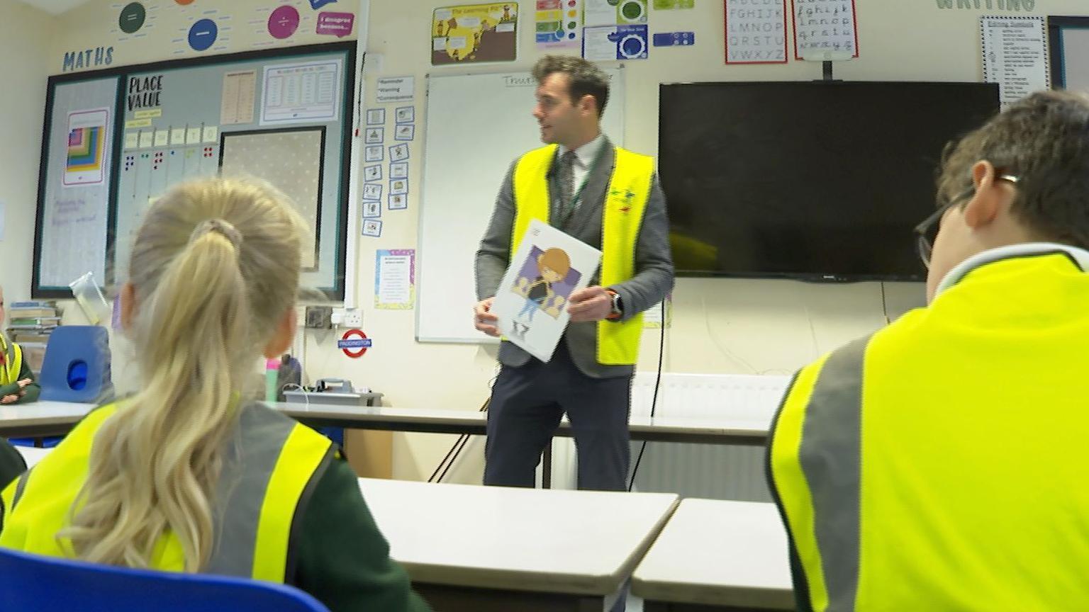 A teacher in a class instructing children on the KiVa Programme. They are wearing high viz vests.