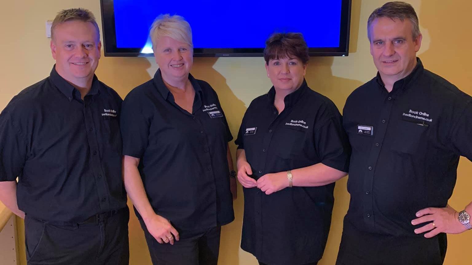 A picture of cinema staff in black shirts - two men on the outside and two women in the middle