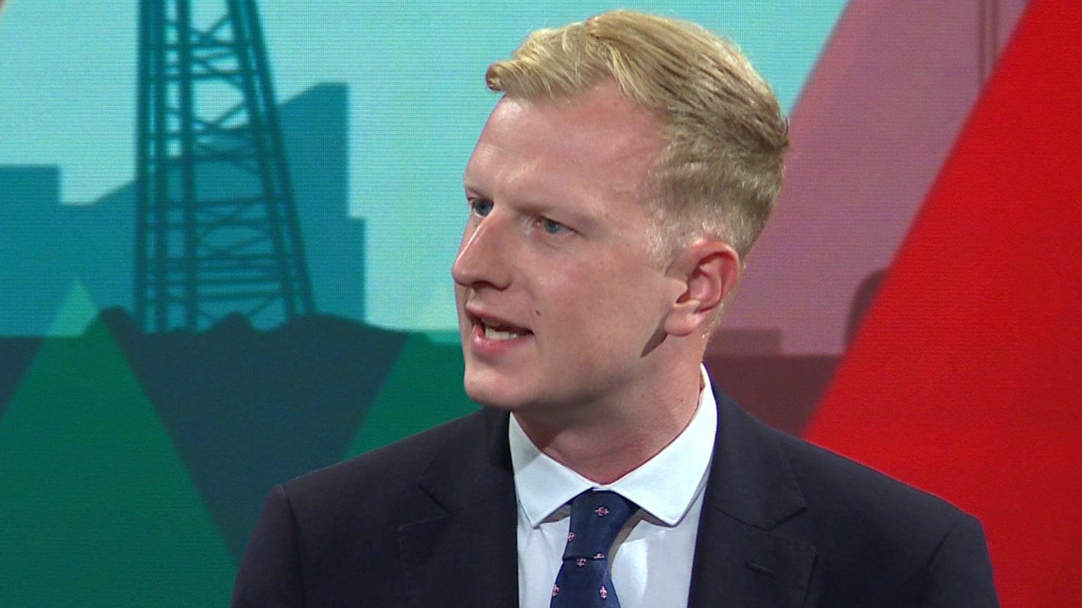 Niall Innes is speaking from the red and blue Politics North studio. He has short blonde hair and is wearing a blue suit.