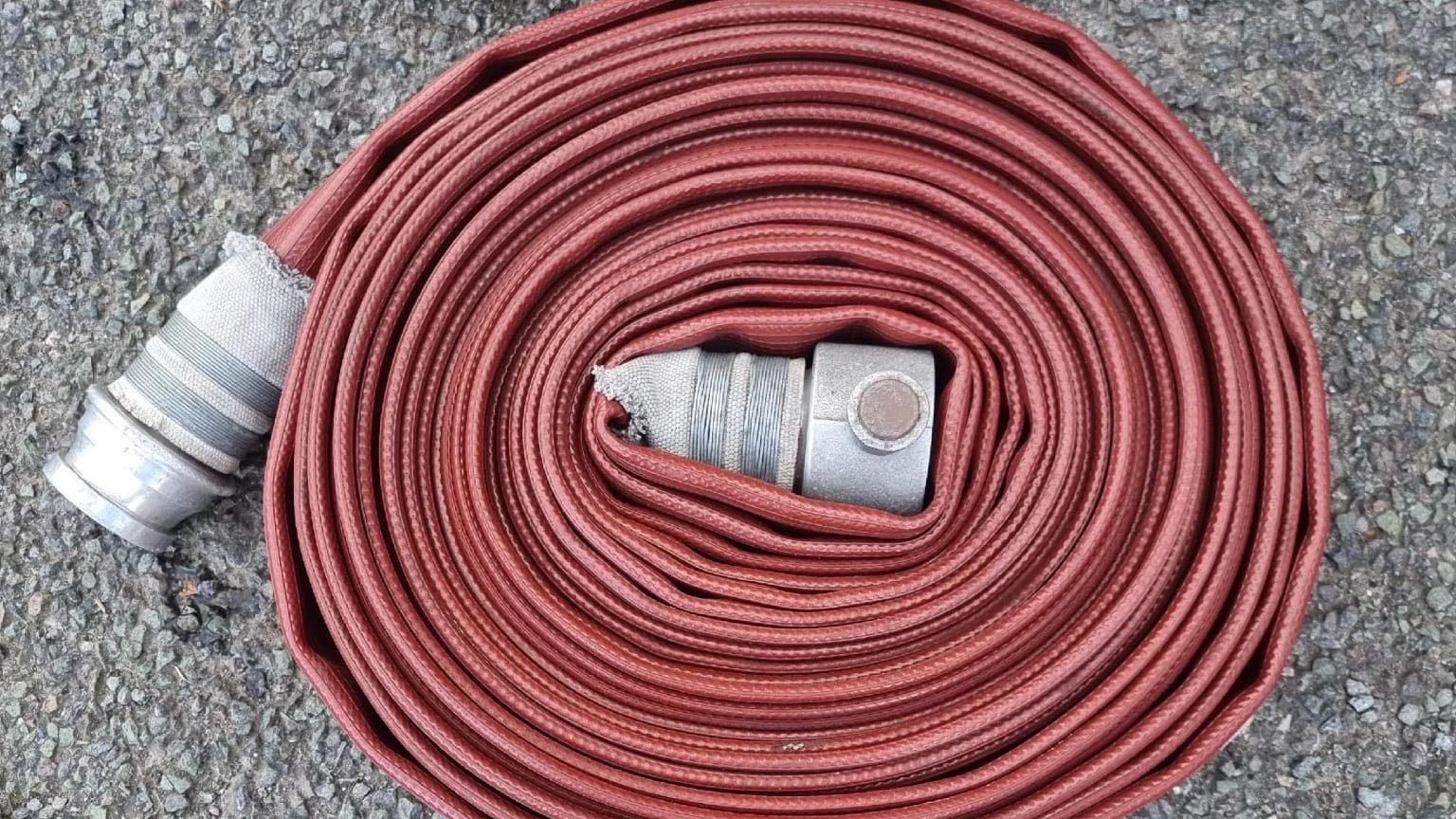 A red fire hose neatly coiled into a tight circular shape laid on the concrete.