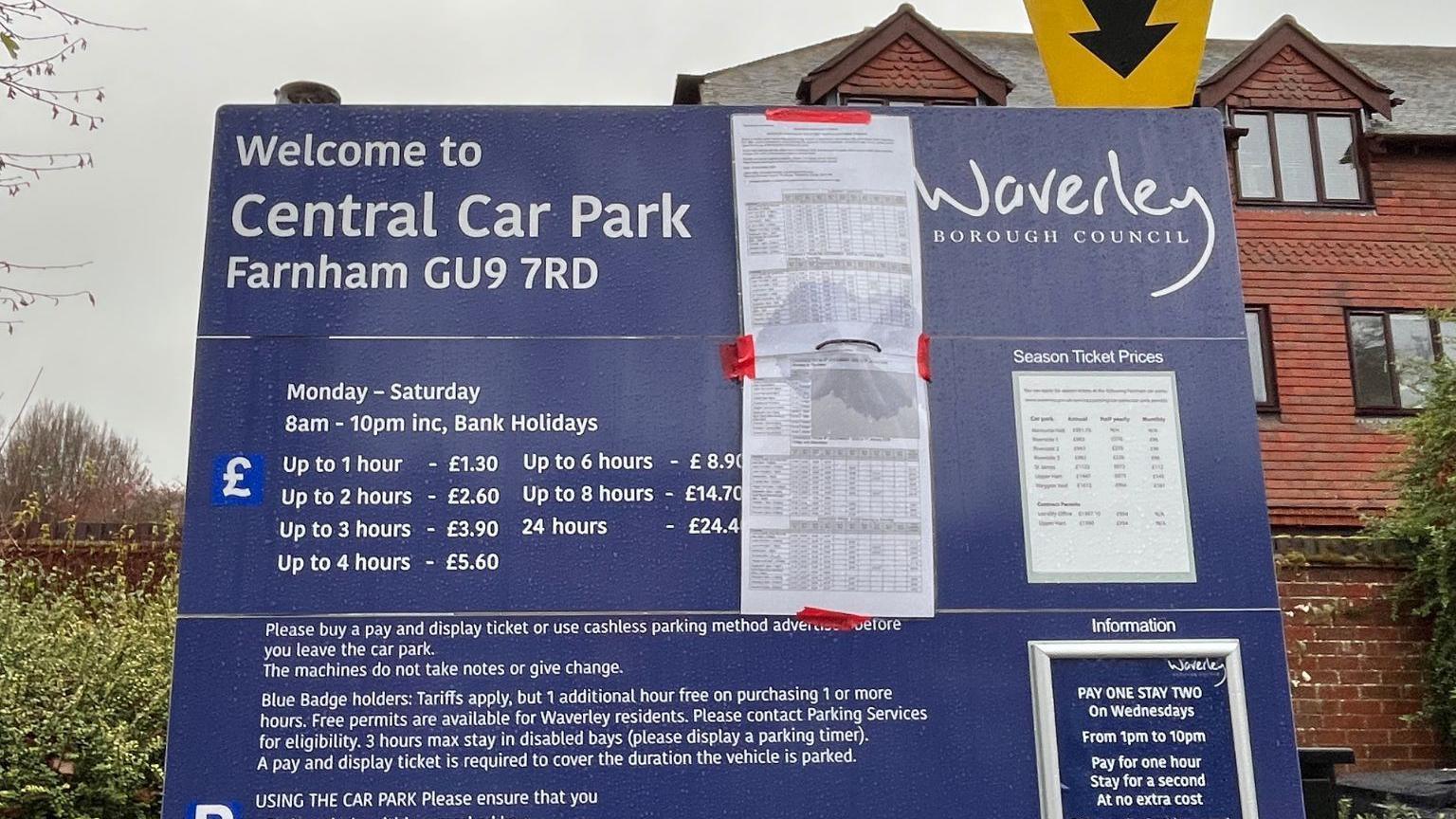 A dark blue sign displaying car parking charges and information in white text