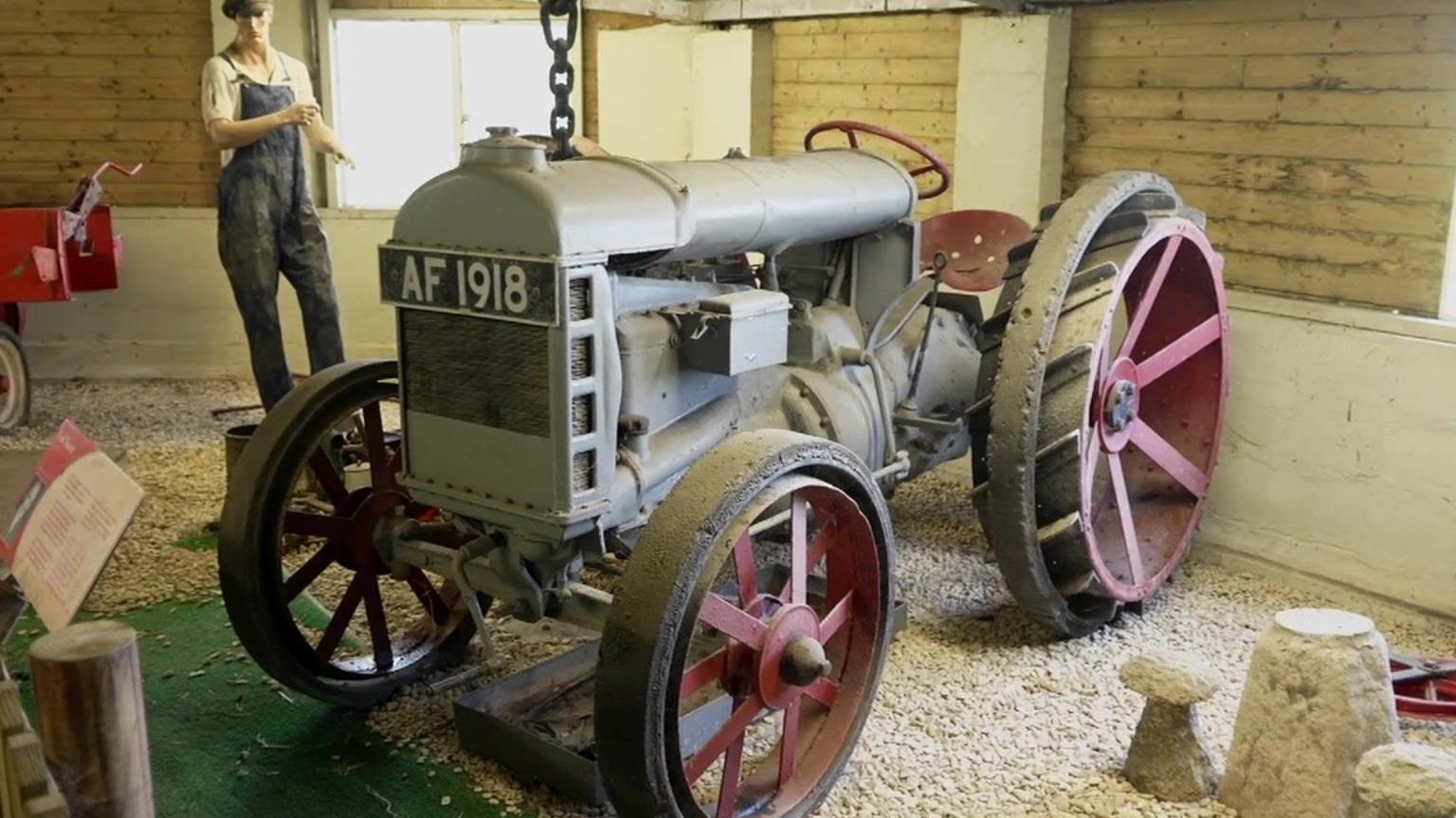 An old grey tractor with metal wheels and solid rubber tyres with a model of a farmer behind.