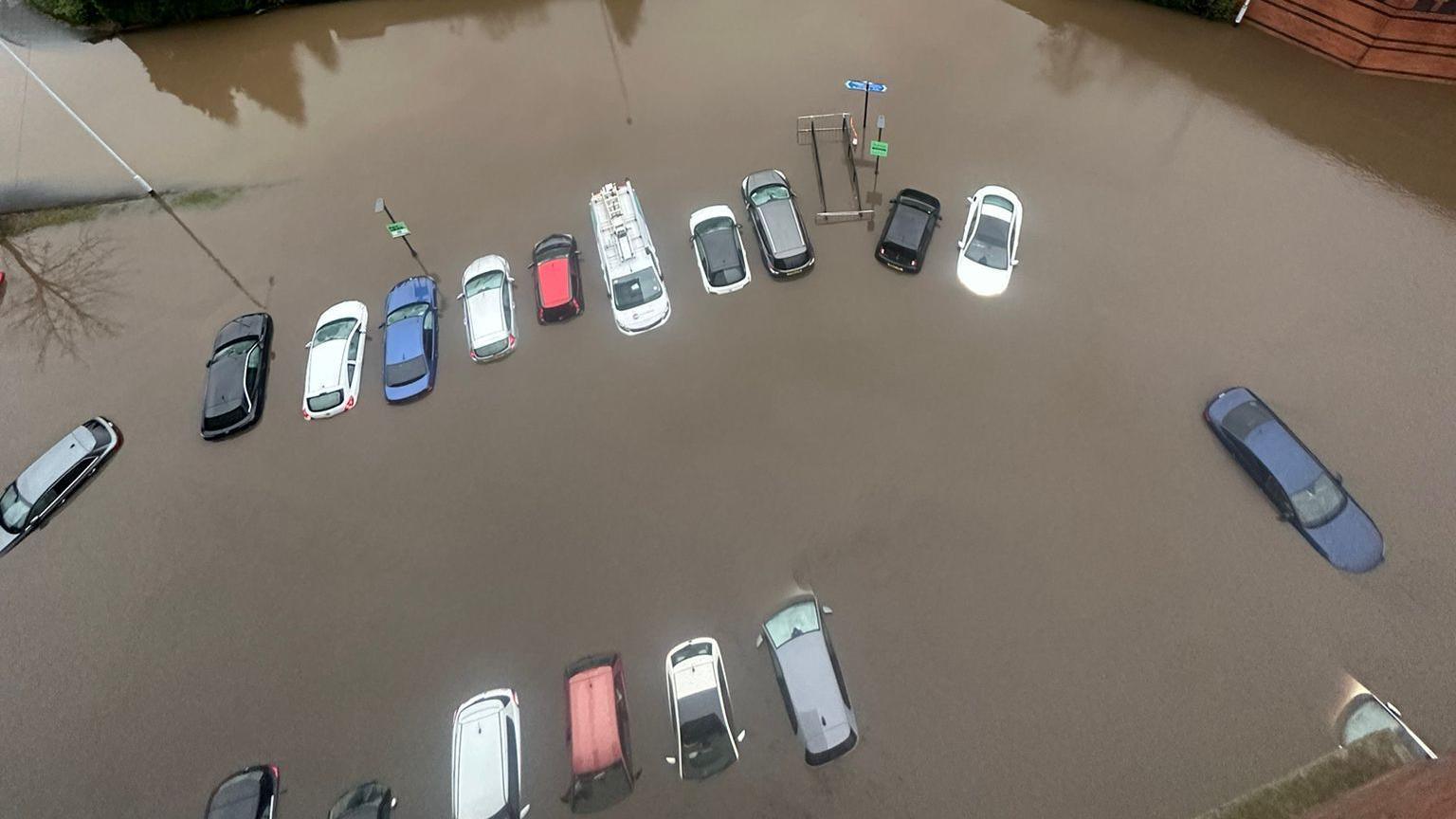 An aerial view from a balcony showing a number of cars partially submerged in brown, muddy floor water with their roofs showing.