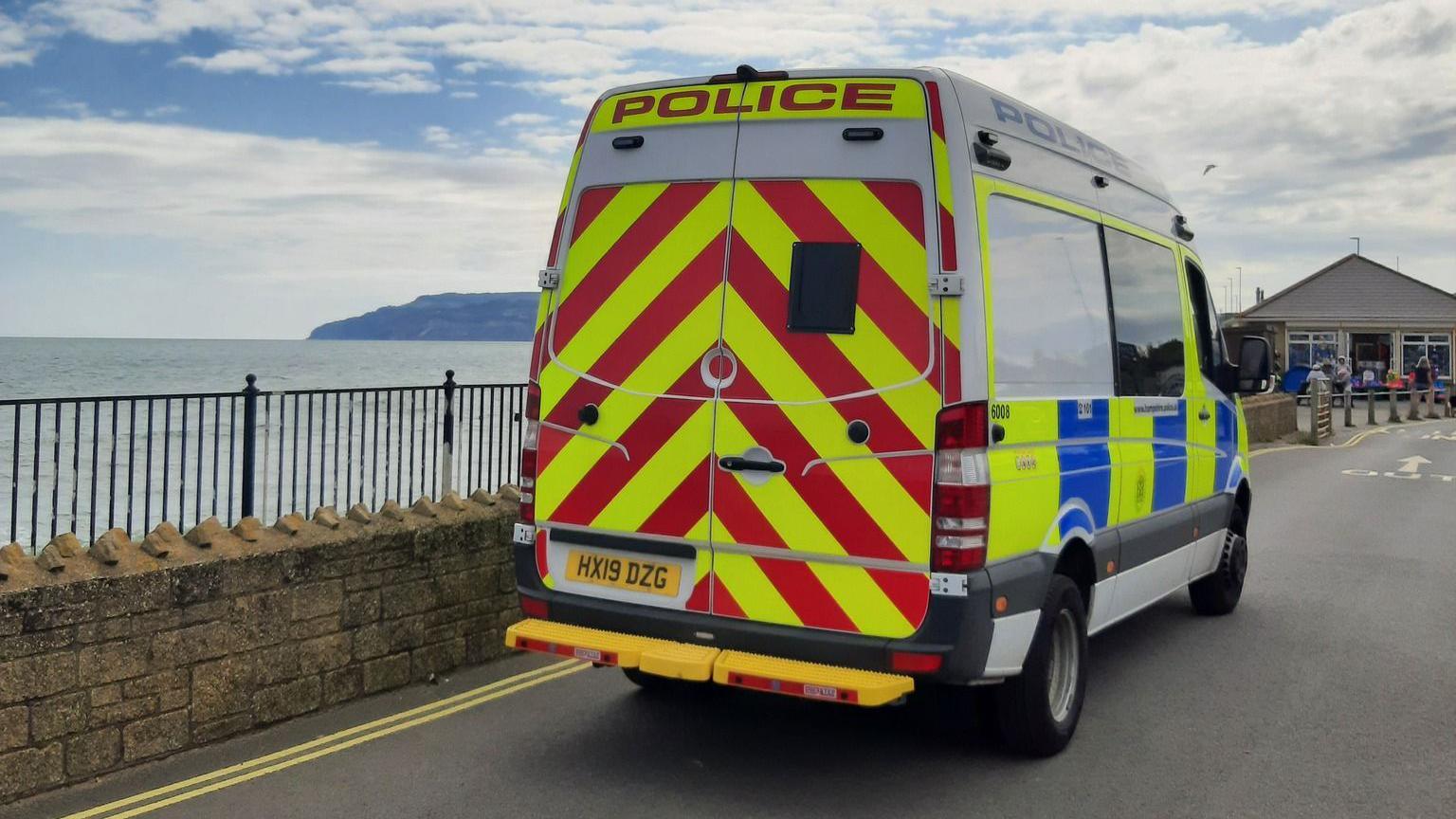 A marked police van is parked by a wall overlooking the sea