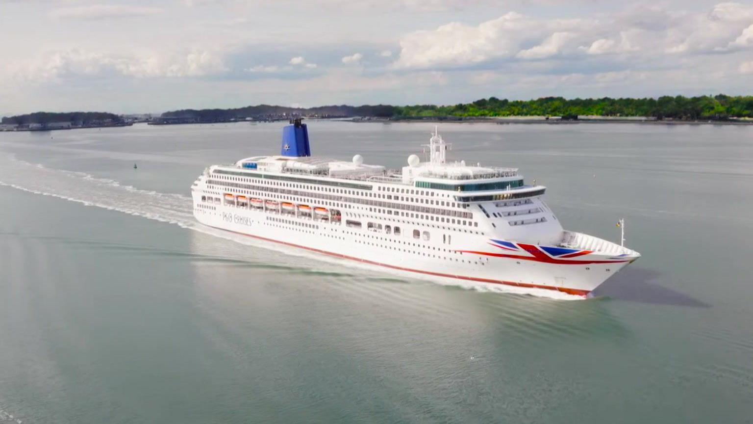 An aerial shot of the cruise ship sailing on the sea. It is predominantly white with some Union Jack livery.