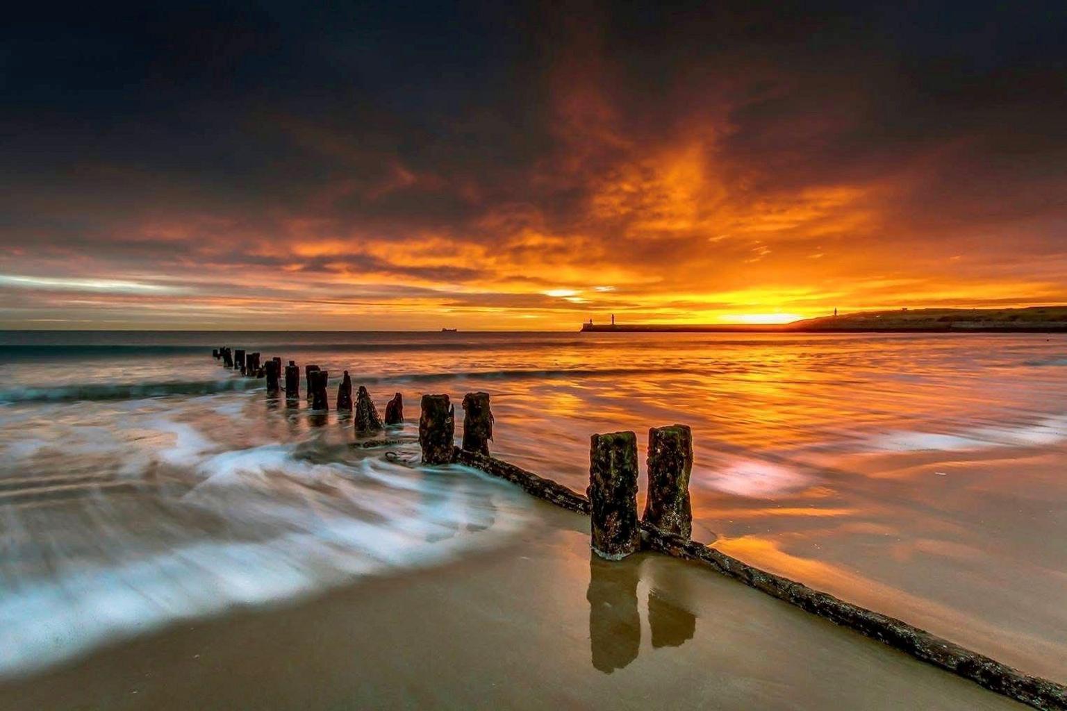 Sunrise on Aberdeen beach, showing wooden spines going into the sea, and an orange glow in the background.