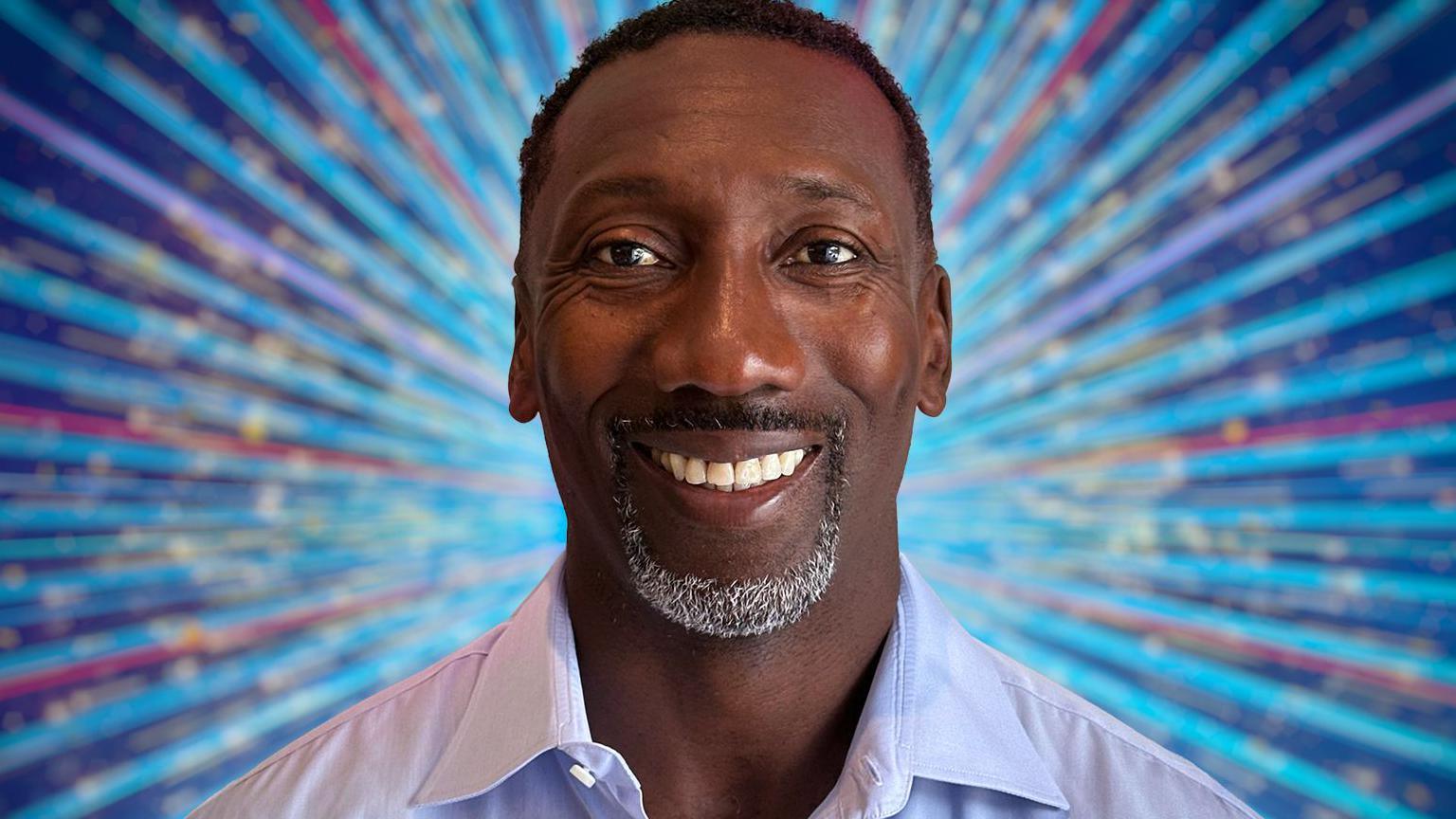 Jimmy Floyd Hasselbaink, he has short black hair and a goatee beard and is wearing an open-necked light blue shirt.