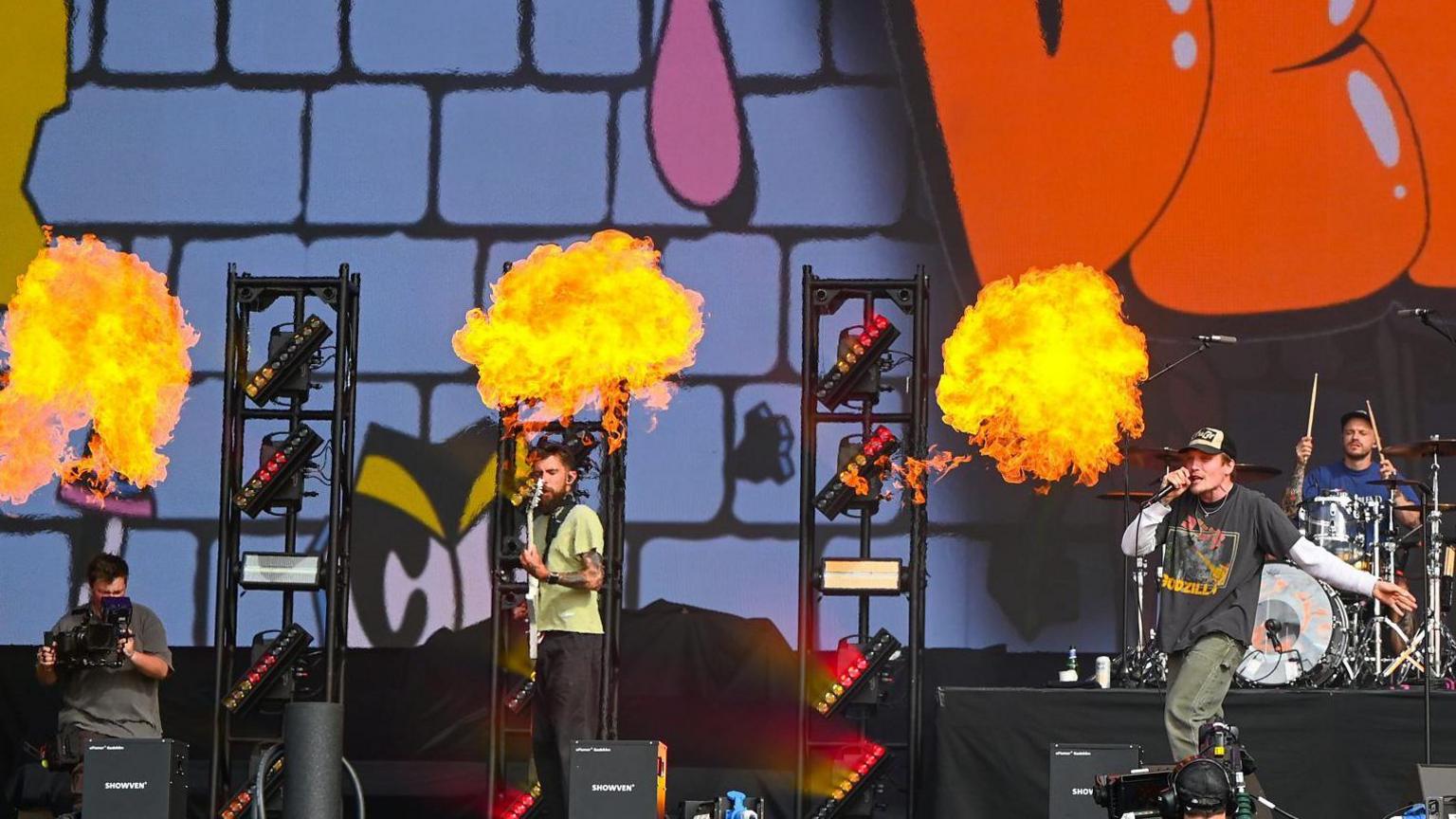 A band on stage with balls of flames burning behind them