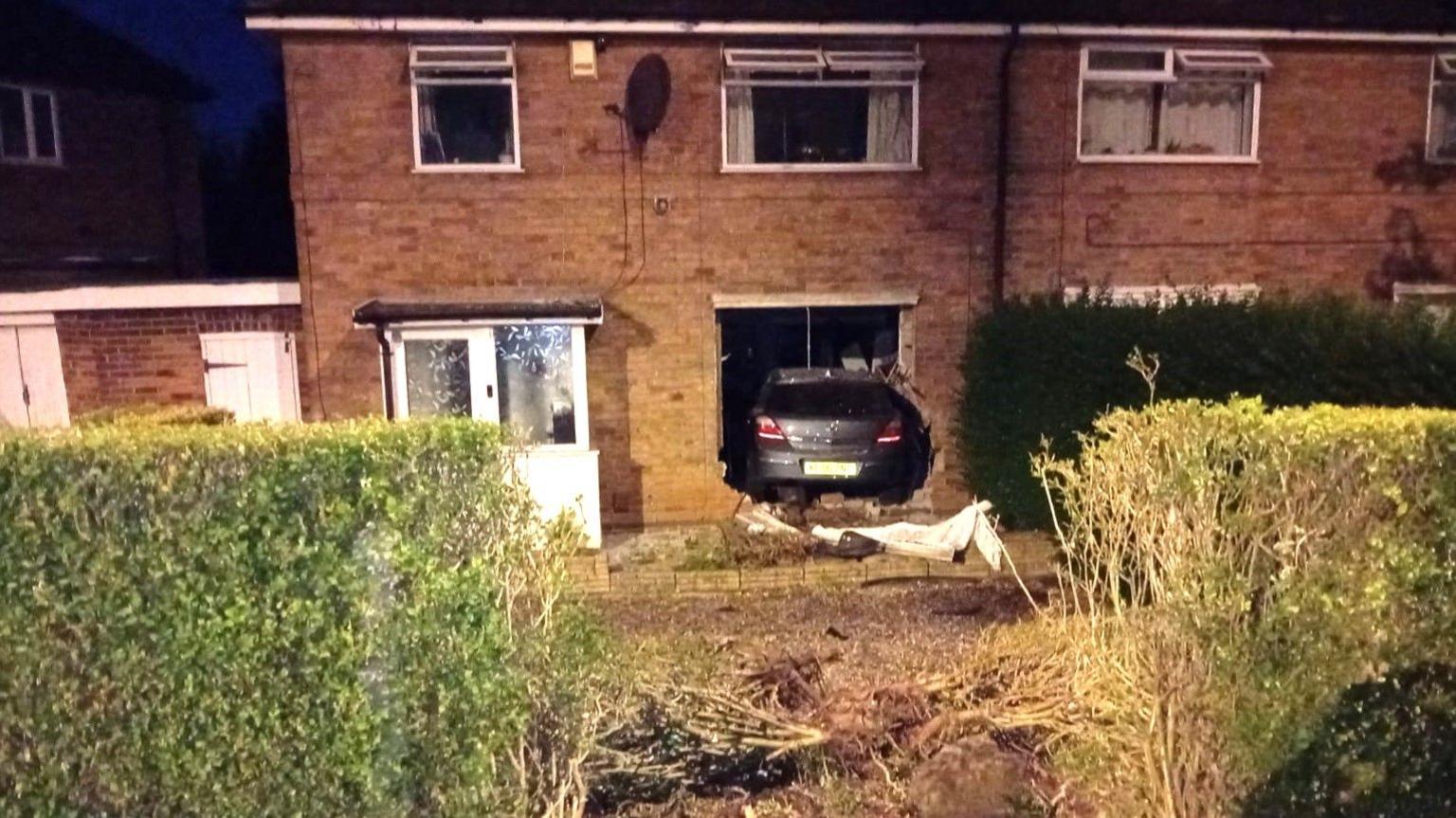 A front view of the house with the car crashed through the main window next to the front door.
