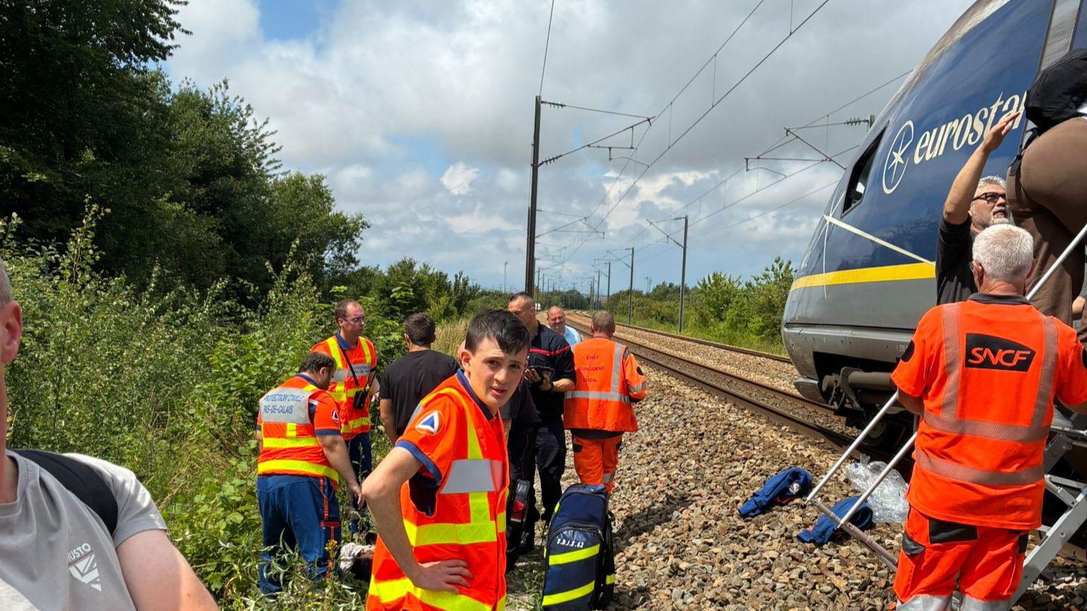 Several men in high-vis clothing are seen helping passengers off the train