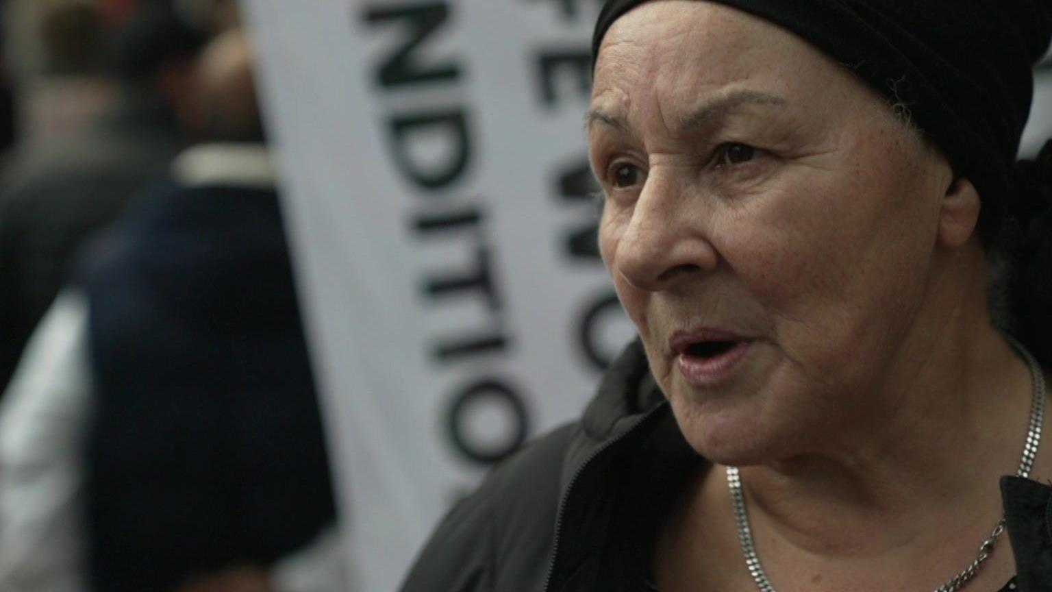 Lorraine Robertson, a woman wearing a black hat and coat and silver necklace as she speaks to a reporter out of shot