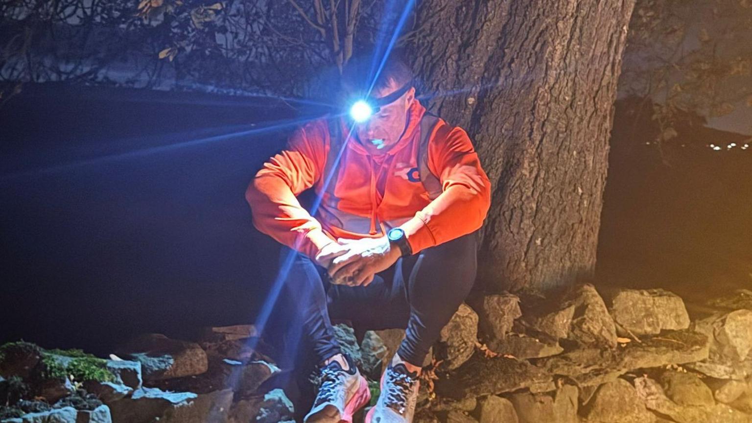 Stephen Melling sits down by a tree as he rests with his head torch on