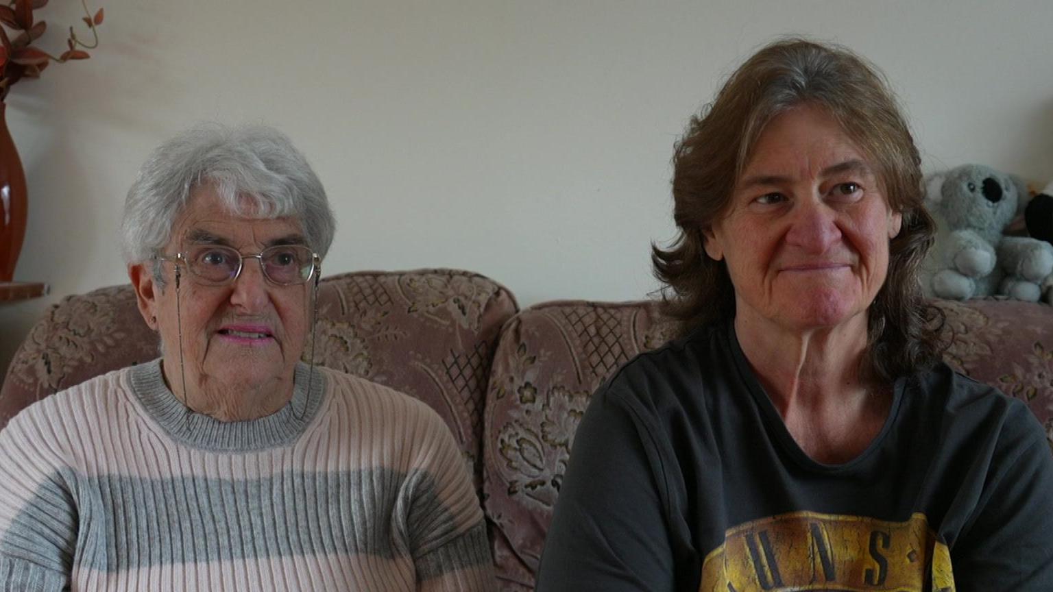 An image of Theresa (on the left) and Sharon Waring (on the right).  Theresa is wearing a pink and grey stripy jumper, while Sharon has on a black Guns N' Roses band t-shirt.  They are both sitting on a pink floral settee.  There is a grey stuffed teddy bear behind Sharon.