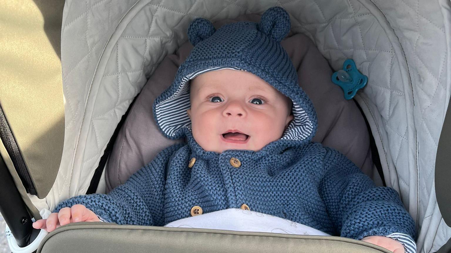 Frankie in a pram wearing a blue jumper and smiling into the camera