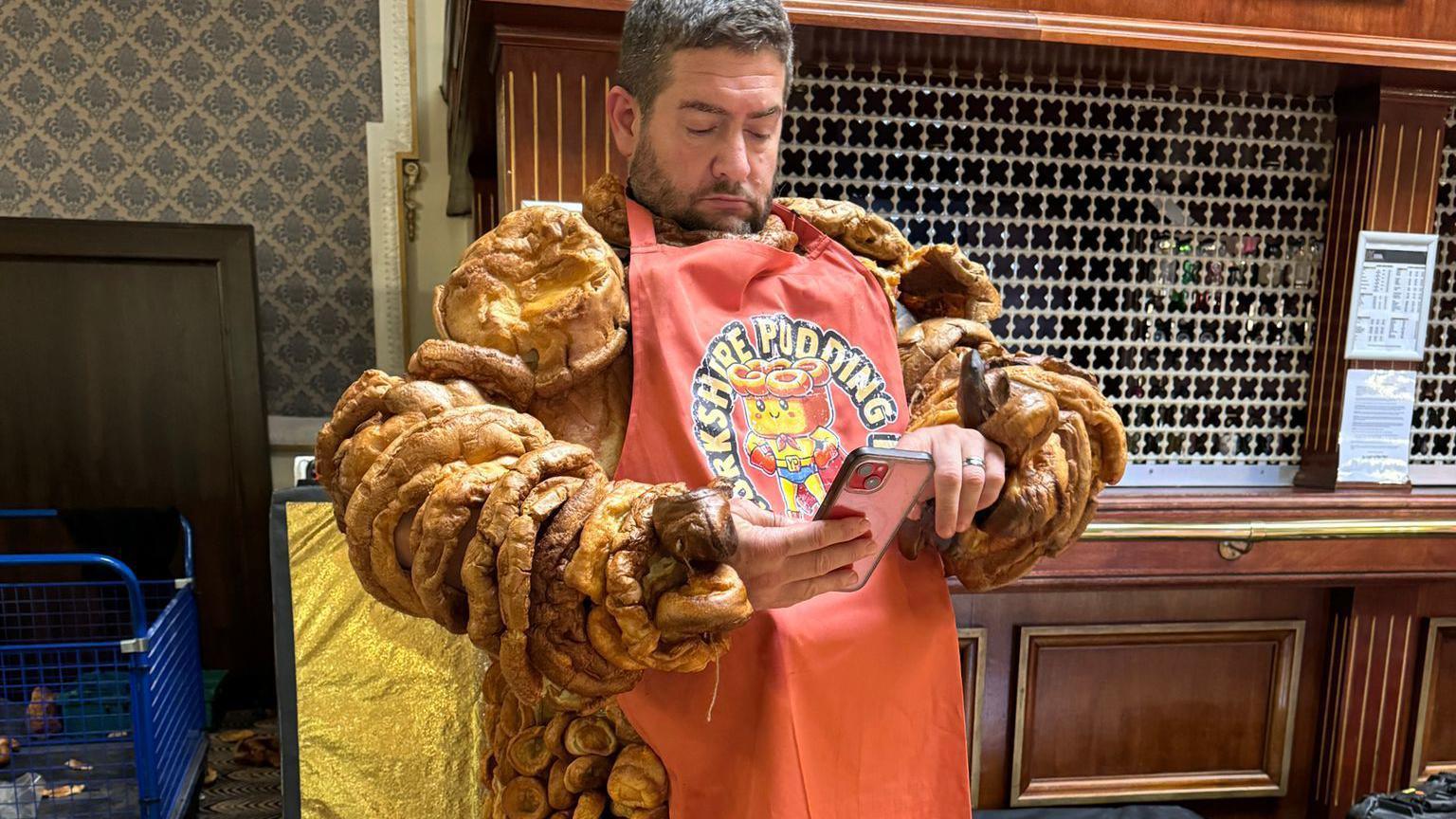 A man with a Yorkshire pudding costume on, tapping on his smartphone.