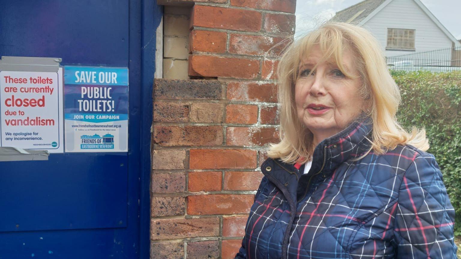 Conservative councillor Jane Lamb standing outside a public toilet that has been closed by vandalism, with a flyer calling for the toilets to be saved posted on the door.