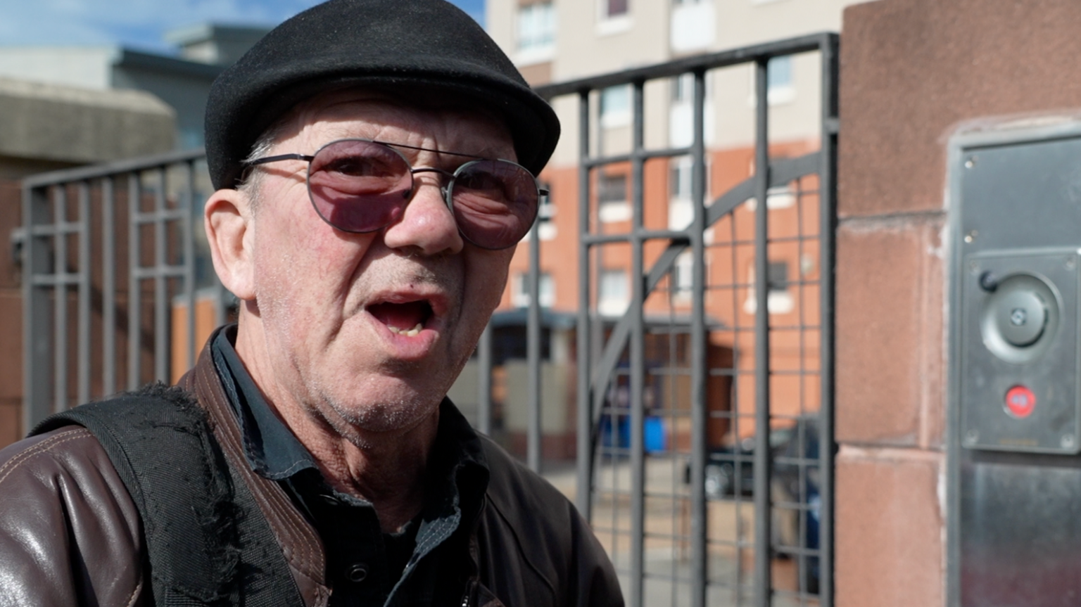 Steve Potter is an older man, wearing a black flat cap and a brown leather jacket. He is standing by a gate and has his mouth open in what looks like surprise.