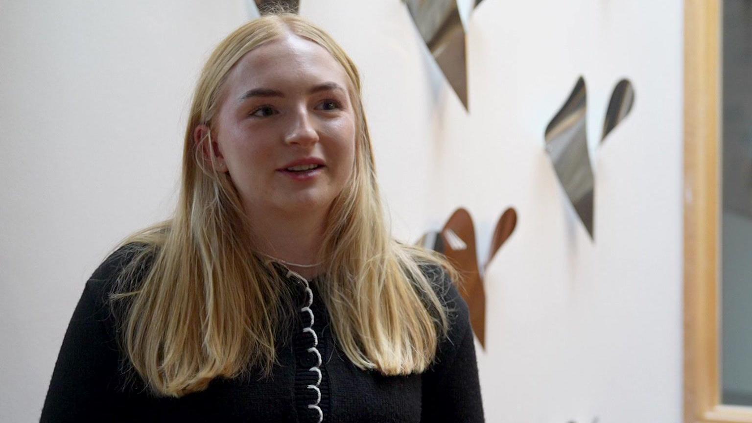 Molly Grainger - merch ifanc gyda gwallt melyn hir mewn top du a gwyn