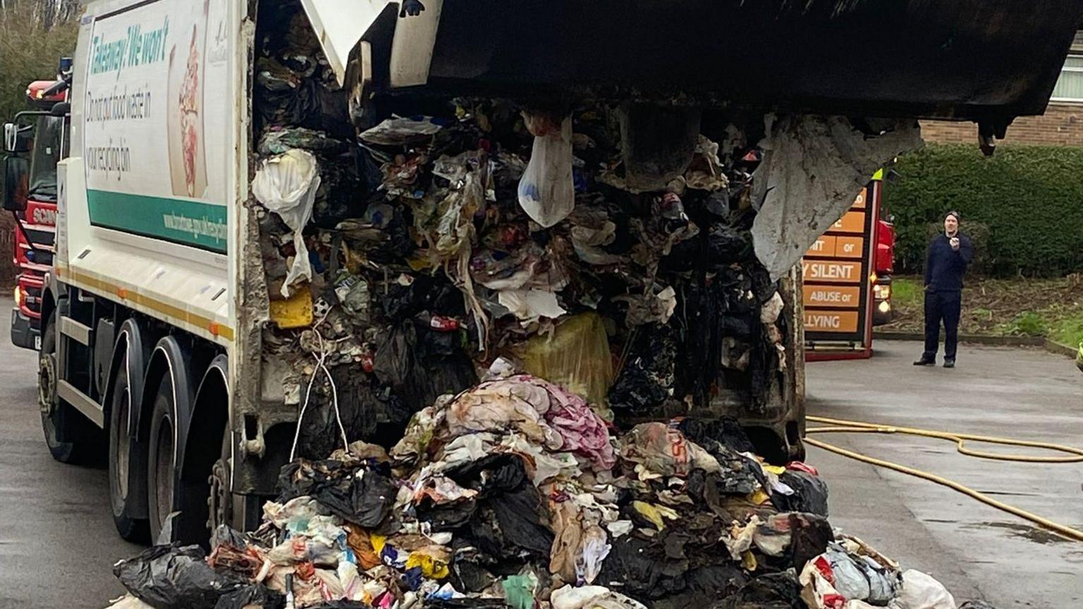 Broxtowe Borough Council waste bin lorry has its back open with rubbish falling out and many rubbish bags are burned from the fire