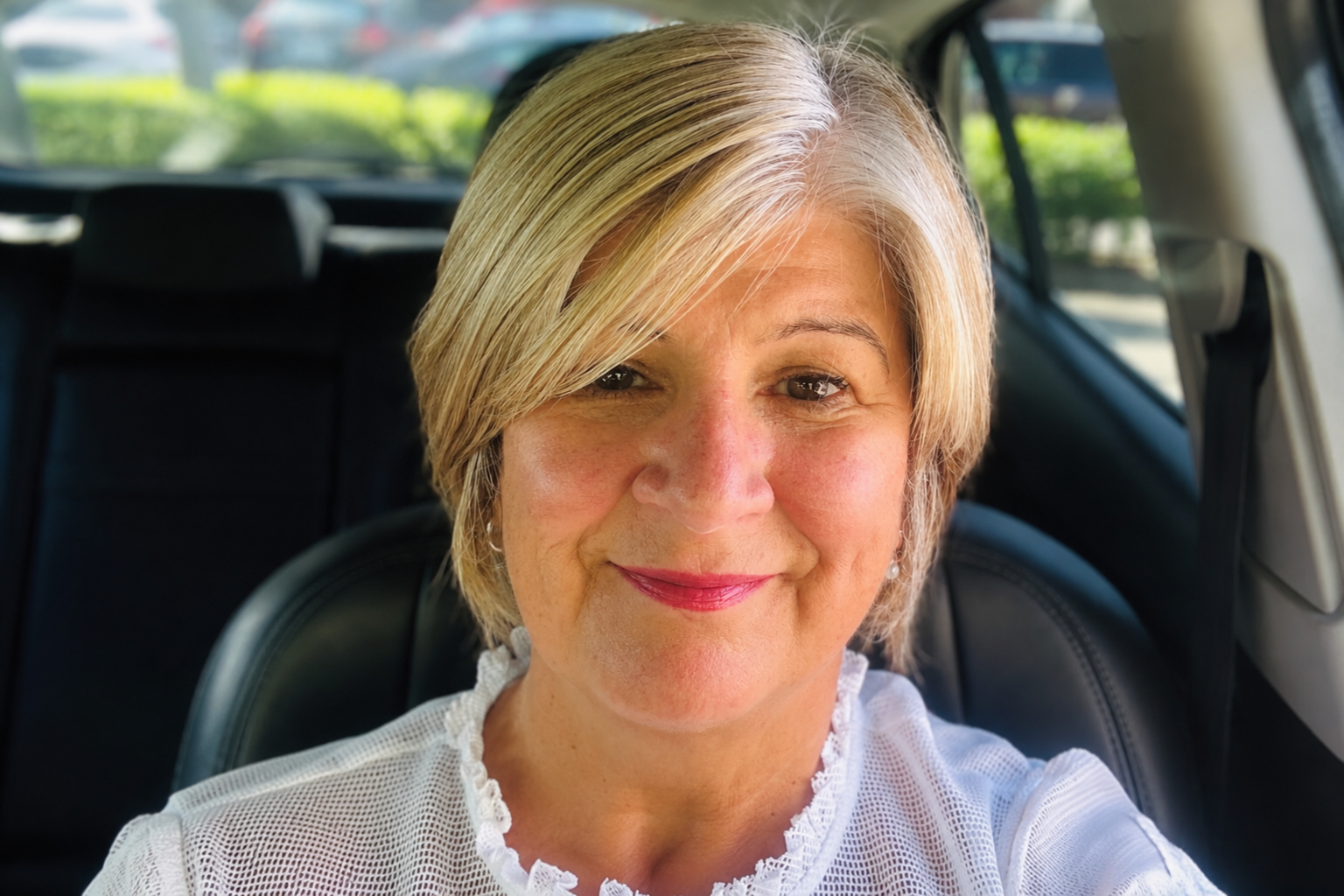 Bernie facing the camera smiling, she has short blonde hair and is wearing a white top.