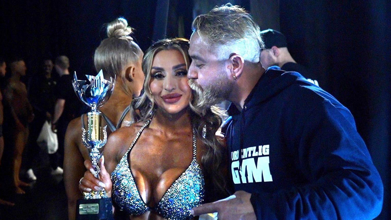 Roya Karimi holding her trophy while her husband, Kamal Jalaluddin, gives her a kiss on the cheek