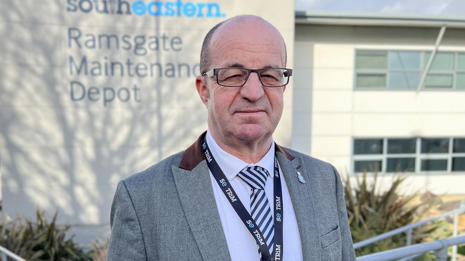 Lee Woolcott-Ellis wearing a suit and lanyard looking to camera with Southeastern's Ramsgate depot behind him