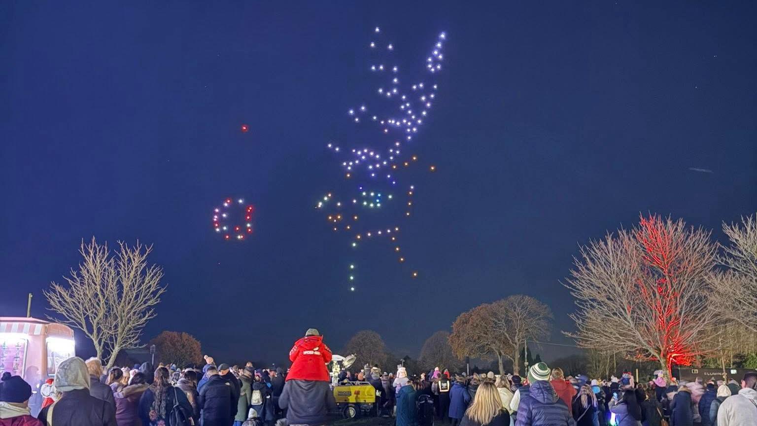 People standing in the Ardingly South of England showground look at an image of a reindeer created in the sky by drones.