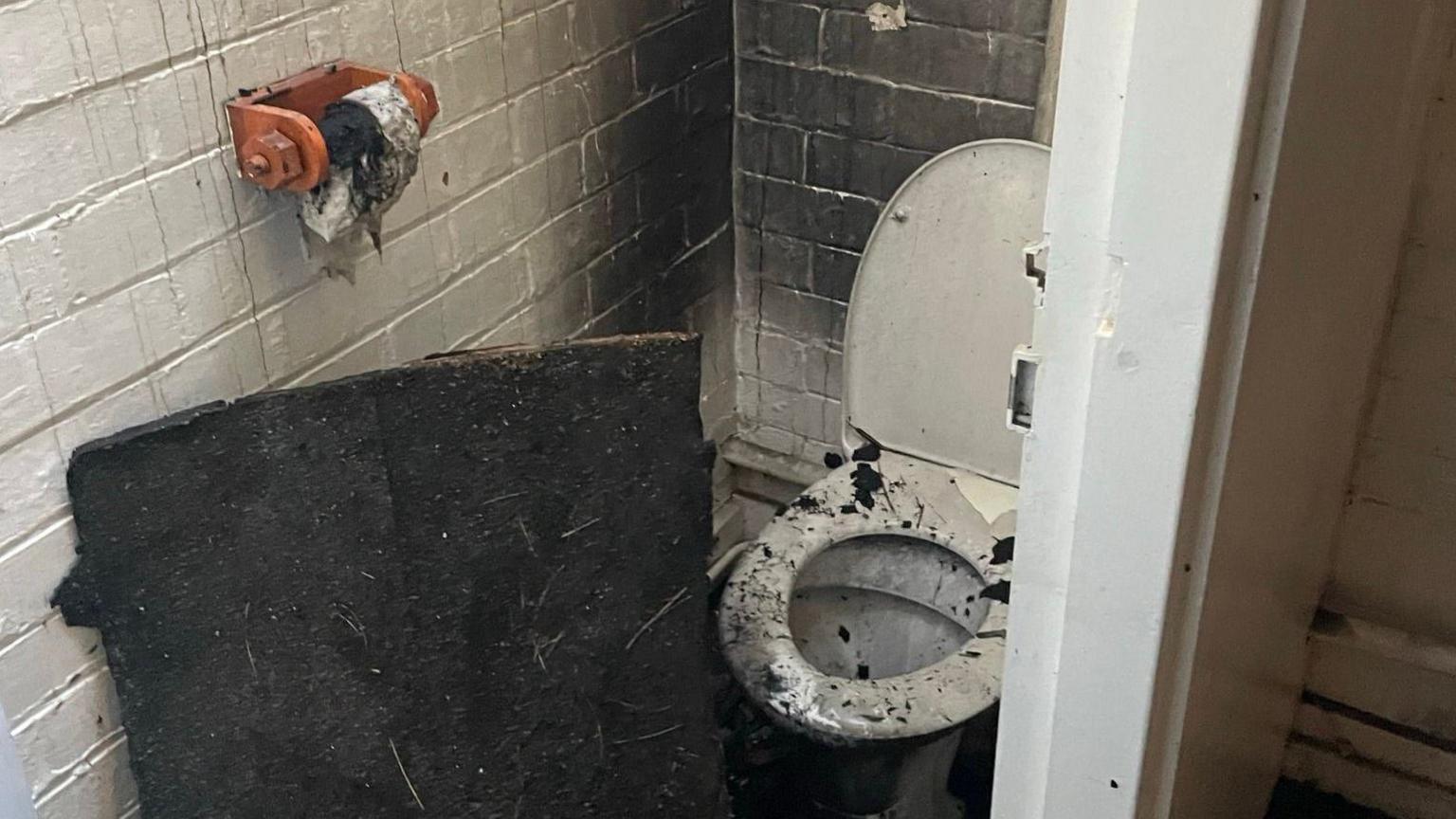 A white toilet covered in bits of roof. The white walls are now black.