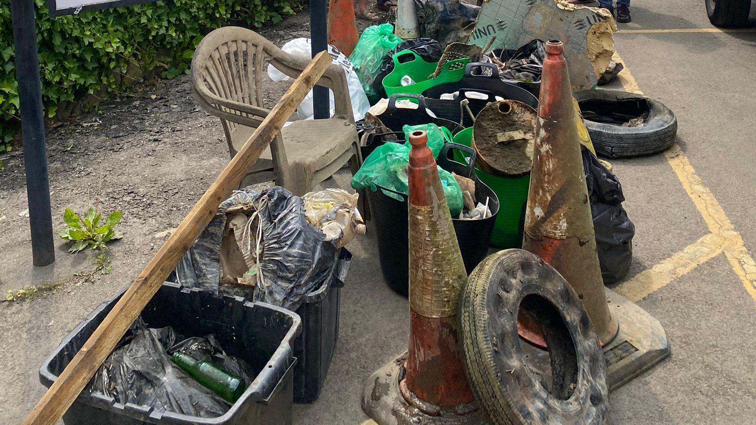 A large pile of rubbish, including a chair, two traffic cones, a plank of wood, a tyre and plastic boxes containing other waste