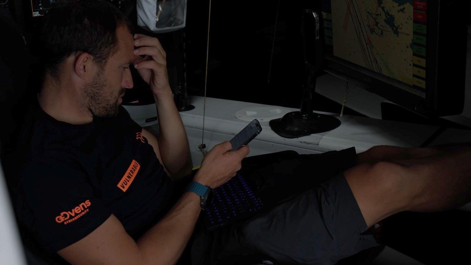 A man wearing T shirt and shorts sits in a chair looking at a device. 